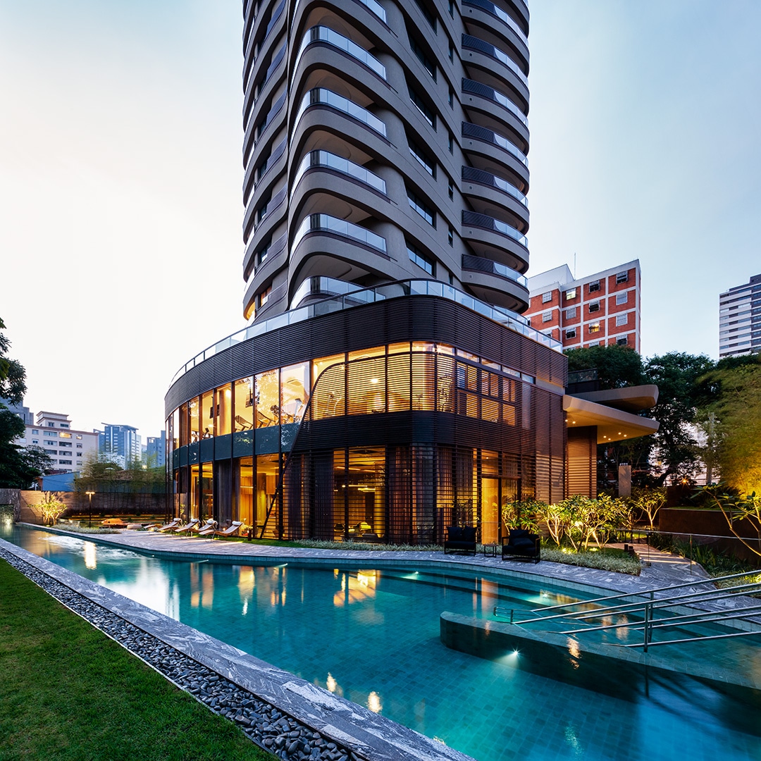 Cyrela by Pininfarina ao entardecer — torre escultural, base de vidro curva e espelho d'água