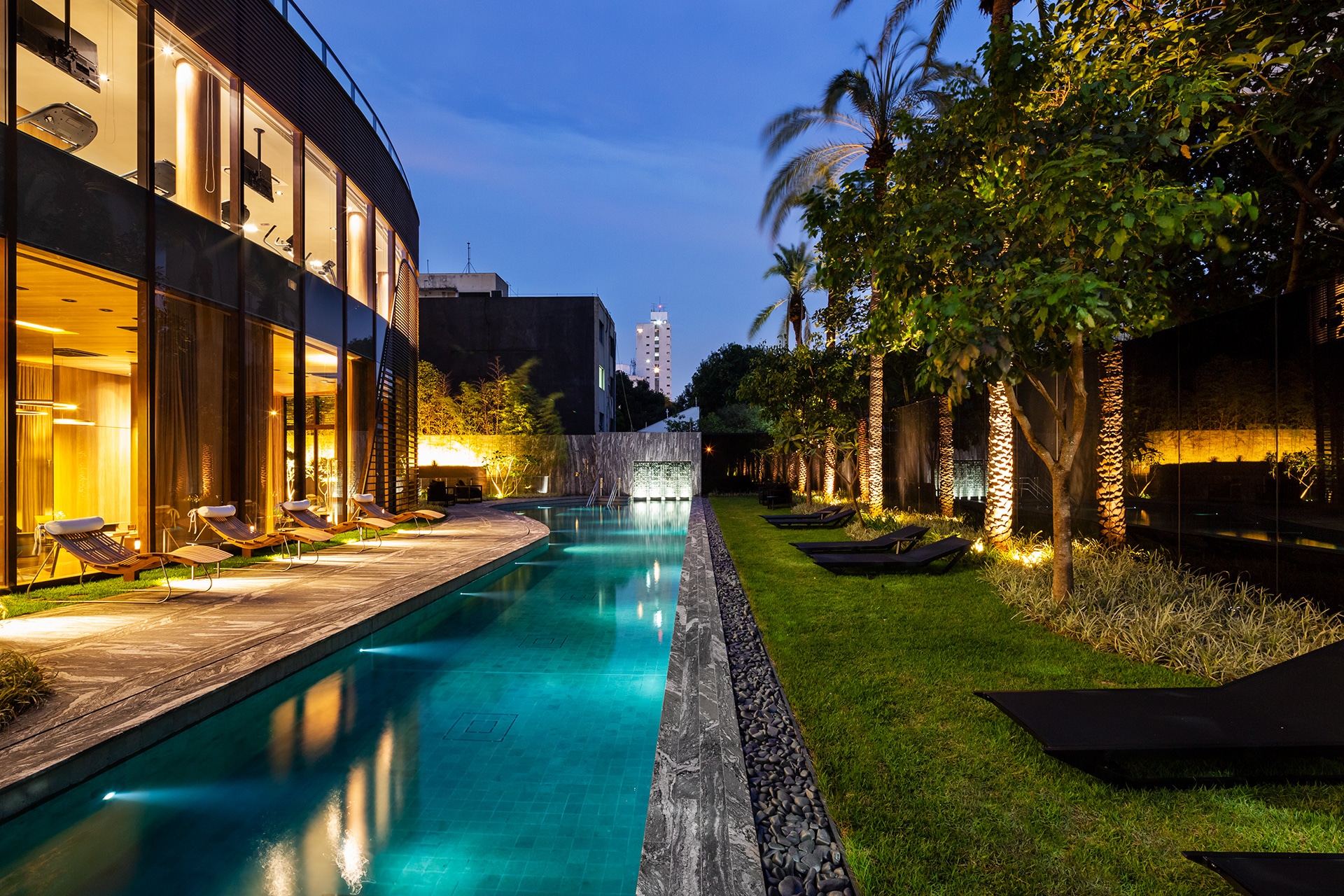 Piscina com raia iluminada ao entardecer, com o edifício ao fundo